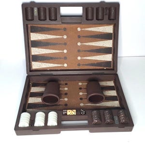 May include: A brown travel case with a backgammon board game inside. The case has a handle and a latch. The board is made of brown and white squares. There are two sets of checkers, one white and one brown, and two dice.