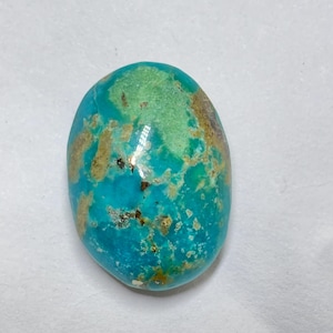 May include: Oval turquoise gemstone with a polished surface. The stone displays a vibrant mix of blue and green hues, with brown and tan matrix patterns. The gemstone is set against a white background.