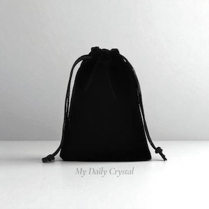May include: A black velvet drawstring pouch with a knotted closure. The pouch is a dark, solid color and is likely used for storing small items. The text "My Daily Crystal" is printed at the bottom of the image.