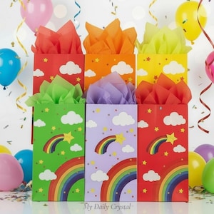 May include: Six colorful gift bags with rainbow, cloud, and star designs. Each bag is filled with tissue paper in coordinating colors. The bags are red, orange, yellow, green, purple, and red. The text "My Daily Crystal" is at the bottom.