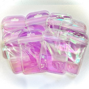 May include: A collection of iridescent, holographic zip-top bags. The bags are a soft pink color with a shimmering, rainbow effect. Each bag has a small hole at the top for hanging. The bags are made of a clear, flexible material.