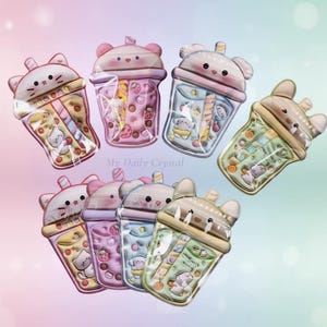 May include: A collection of kawaii-style drink charms in various pastel colors. Each charm is shaped like a bubble tea cup with a cute animal face on top. The cups are filled with colorful illustrations of fruits and animals.