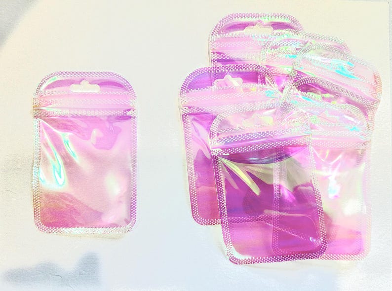 May include: Several iridescent pink, clear, and purple pouches with a zip closure and a small hole for hanging. The pouches are made of a shiny, transparent material. The pouches are empty and ready to be filled.