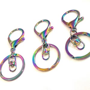 May include: Three iridescent keychains with lobster claw clasps and key rings. The keychains have a rainbow finish, displaying hues of purple, green, and gold. The key rings are oval-shaped and attached to the clasps.