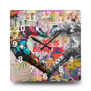 May include: Square wall clock with a colorful graffiti design. The clock face features two hands forming a heart shape, with the words "LIFE IS BEAUTIFUL" in red. The clock hands are black, and the numbers are white.
