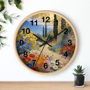 Puede incluir: Un reloj de pared redondo con marco de madera clara. La esfera del reloj presenta una colorida escena de jardín con un camino, flores y árboles. Las manecillas negras indican la hora. El reloj mide aproximadamente 30 cm de diámetro.