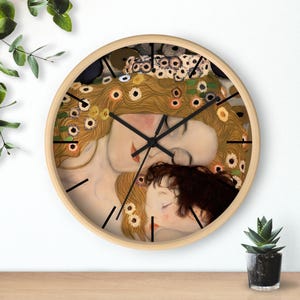 Puede incluir: Reloj de pared redondo con marco de madera clara. La esfera del reloj presenta un detalle de una pintura con figuras en tonos cálidos de oro, beige y marrón. Agujas y marcadores negros.