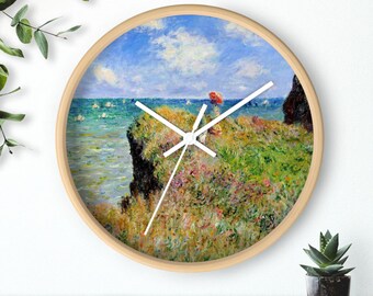 Könnte beinhalten: Runde Wanduhr mit hellem Holzrahmen. Das Zifferblatt zeigt ein Landschaftsgemälde mit einer Person, die einen roten Regenschirm hält. Das Gemälde hat blaue, grüne und gelbe Farbtöne.
