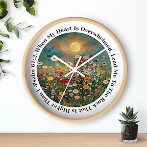 Op de afbeelding: Een ronde wandklok met een licht houten frame. De wijzerplaat toont een kleurrijk bloemenschilderij met een heldere gele zon en de tekst "When My Heart Is Overwhelmed, Lead Me To The Rock That Is Higher Than I - Psalm 61:2-".