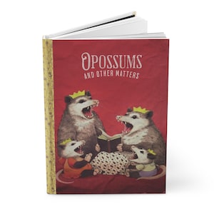 May include: Hardcover journal with a red cover featuring the title "Opossums and Other Matters." The cover art depicts four opossums wearing crowns, with open mouths, and reading a book. The journal's spine is gold with a floral pattern.