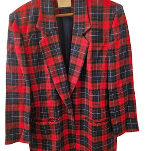May include: A red, black, and navy plaid blazer with a single-button closure. The blazer is hanging on a wooden hanger. The jacket has two front pockets and a navy blue lining.
