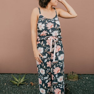 May include: A person wearing a dark blue floral print pajama set with a pink ribbon tie at the waist. The pajama top has thin straps and the pants are wide-legged.
