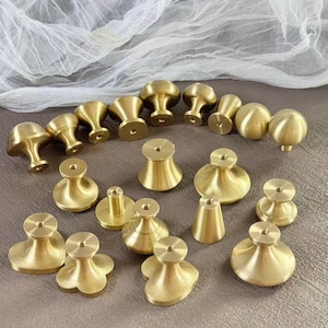 May include: A collection of brass cabinet knobs in various shapes, including mushroom, round, and flower designs. The knobs are arranged on a neutral surface, showcasing their polished, golden finish. These decorative hardware pieces are ideal for furniture upgrades.