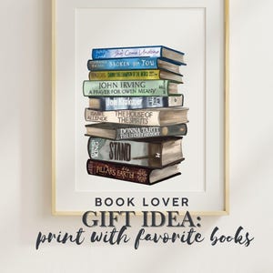 Puede incluir: Una impresión enmarcada que muestra una pila de libros, con títulos como "She's Come Undone" y "Stand". La impresión incluye el texto "Book Lover" y "Gift Idea: print with favorite books".