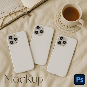 Puede incluir: Tres fundas blancas para teléfono con detalles negros de cámara están dispuestas sobre una superficie beige. Una taza de té se encuentra sobre un posavasos blanco, y un par de gafas descansa cerca de un libro abierto. La palabra "Mockup" se muestra.