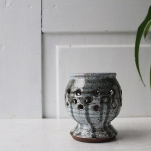 May include: A white ceramic candle holder with a brown base and a pattern of holes around the sides. The candle holder is sitting on a white surface.