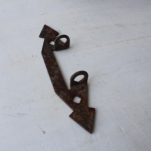 May include: A rusty metal hinge with a rectangular shape, two circular loops, and a pointed end. The hinge is likely vintage or antique, with visible signs of wear and age.