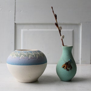 May include: Two ceramic vases, one with a blue and white geometric pattern and the other a light blue with a brown feather design.
