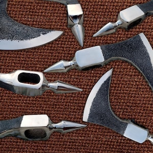 Op de afbeelding: Een assortiment metalen bijlkoppen met een getextureerde zwarte afwerking op de bladen en gepolijste zilveren accenten. De bijlen hebben een puntige punt aan de tegenovergestelde kant van het blad. De items zijn gerangschikt op een bruin, getextureerd oppervlak.