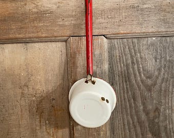 May include: A vintage enamel ladle featuring a white bowl and a long red handle. The metal surface shows signs of wear with visible rust spots along the handle and at the connection point where the bowl meets the handle, indicating age and use.