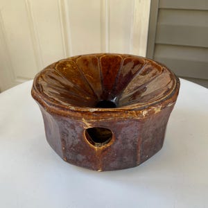 May include: A brown glazed ceramic mold with a fluted top and a hole in the bottom. The mold is designed for baking.