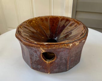 May include: A brown glazed ceramic mold with a fluted top and a hole in the bottom. The mold is designed for baking.