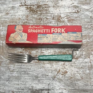 May include: A metal spaghetti fork with a green handle and a manual crank mechanism, accompanied by a red rectangular box featuring the text Automatic SPAGHETTI FORK, along with illustrations showing the steps to dig, crank, and eat.