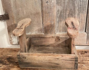 May include: A rustic wooden shoe rack with two shoe horns. The rack is made of weathered wood and has a rectangular shape. The shoe horns are made of wood and have a curved shape.