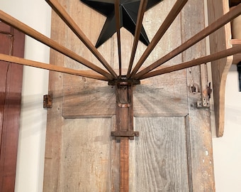 May include: A wall-mounted wooden drying rack featuring a central vertical support and multiple radiating horizontal arms. The rack is constructed from natural brown wood and includes a metal hinge mechanism at the center point where the arms pivot.