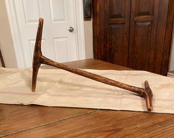 May include: A rustic wooden tool with a long handle and a T-shaped head. The tool is weathered and has a natural brown color.