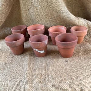 May include: Eight terracotta flower pots of various sizes, arranged on a burlap surface.