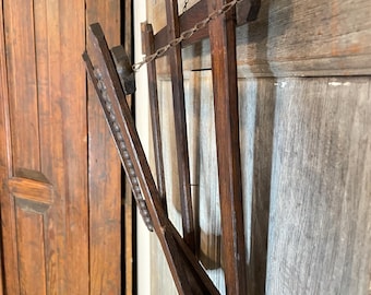 May include: A dark brown wooden drying rack with a chain, mounted on a light brown wooden door. The rack has multiple vertical slats and a folding design. The rack is made of wood and has a rustic appearance.