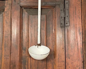 May include: A white enameled metal ladle with a long, straight handle. The ladle features visible signs of wear, including chipped enamel and exposed dark metal along the rim of the bowl and the connection point between the handle and the bowl.