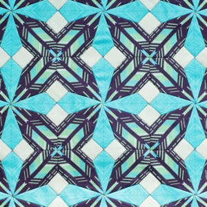 May include: A quilt with a geometric pattern of blue, white, and green triangles and squares. The quilt is made of fabric with a striped pattern.