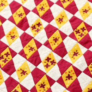 May include: A quilt with a diamond pattern in shades of burgundy, yellow, and white. The diamonds are decorated with small floral designs in burgundy.