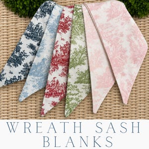 May include: A collection of five fabric sash blanks for wreaths, each featuring a distinct toile de jouy pattern in navy blue, light blue, red, green, and pink on a white background. The sashes are pointed at the ends and arranged in a fan shape.