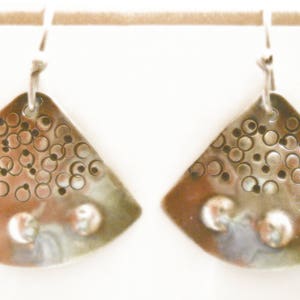 May include: A pair of silver earrings with a textured, circular pattern. The earrings are shaped like a fan and have a slightly iridescent finish.