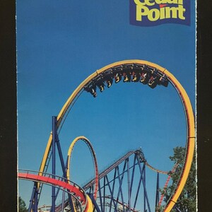 Może przedstawiać: Przewodnik po zabawie 1997 dla parku rozrywki Cedar Point. Okładka przedstawia błękitne niebo z żółtym i niebieskim rollercoasterem na pierwszym planie. Kolejka górska jest w ruchu z ludźmi, którzy z niej korzystają.