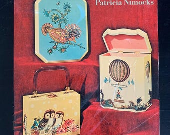 以下が含まれることがあります： パトリシア・ニモックス著「The Craft of Decoupage」というタイトルの本。表紙には、鳥と花のデザインが施された小さな箱、熱気球のデザインが施された大きな箱、フクロウと花が描かれたハンドバッグの3つのデクーパージュ作品が掲載されています。