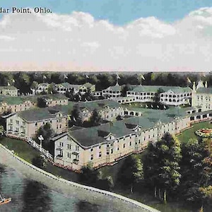 Op de afbeelding: Een luchtfoto van een groot, wit gebouw met meerdere vleugels en een uitgestrekt gazon. Het gebouw is omgeven door bomen en een waterpartij. De tekst "The Cedars, Cedar Point, Ohio." is zichtbaar bovenaan de afbeelding.