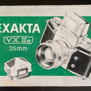 Op de afbeelding: Vintage Exakta VX IIa 35mm cameradoos met een groen en wit ontwerp. De doos bevat een illustratie van de camera en een aparte zoeker. De tekst "EXAKTA VX IIa 35mm" is prominent aanwezig.