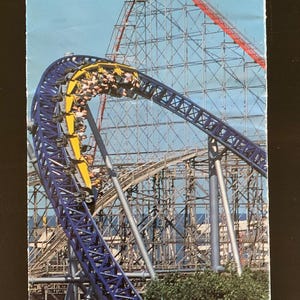 Może przedstawiać: Broszura parku rozrywki Cedar Point w Sandusky, Ohio, z kolejką górską z niebieskimi i żółtymi torami. Tekst brzmi "Guide & Map to Fun!" i "This is your 2001". Logo Cedar Point zawiera Snoopy.