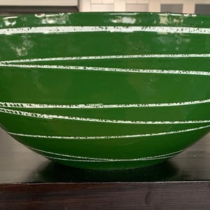 Puede incluir: Un cuenco grande y verde brillante con rayas blancas horizontales pintadas a mano. El cuenco es redondo y tiene una amplia abertura. Este cuenco decorativo es adecuado para servir o exhibir.