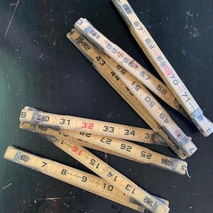 May include: A set of six vintage wooden folding rulers. The rulers are yellowed with age and have black and red markings. The rulers are all different lengths, with the longest being about 71 inches.