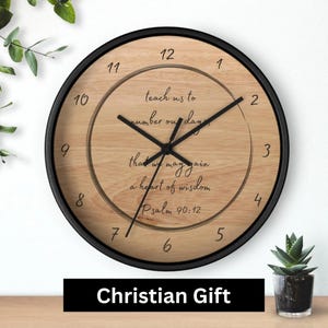 May include: Round wall clock with a black frame and a light wood grain face. The clock hands are black. The face has black numbers and the text "teach us to number our days, that we may gain a heart of wisdom, Psalm 90:12." The bottom of the image has the text "Christian Gift."