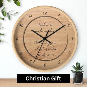 May include: A circular wooden wall clock with black hands and numerals. The clock face has the text "teach us to number our days that we may gain a heart of wisdom Psalm 90:12." The words "Christian Gift" are at the bottom.