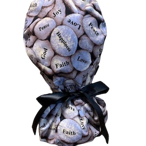 May include: A scrub cap featuring a pattern of light blue stones with words like "Love", "Faith", and "Happiness" printed on them. The cap is tied with a black ribbon. The cap is designed for medical professionals.