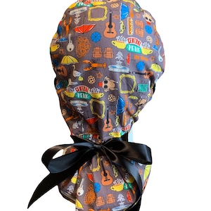 May include: A gray scrub cap with a black bow. The cap is patterned with colorful illustrations of umbrellas, guitars, coffee cups, and the Central Perk logo. The bow is tied at the back of the cap.