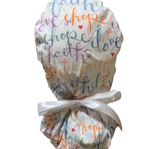 May include: White scrub cap with a colorful script design featuring the words "faith, hope, love" and small crosses and hearts. The cap is tied with a white satin ribbon.