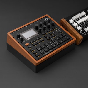 Puede incluir: Un dispositivo de producción de música electrónica negro y marrón con la palabra "Digitakt" en la parte delantera. El dispositivo tiene una pantalla, botones y perillas. El dispositivo está sobre una superficie negra.